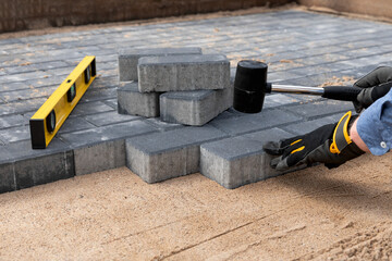 Construction worker laying cement pavement on a walkway with gloves and rubber hammer. House improvement.