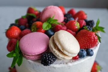 Birthday or anniversary cake with cream cheese frosting decorated with macaroons, fresh raspberries, strawberries, blackberries and blueberries. 