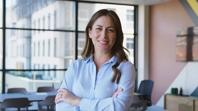 Portrait of smiling mature businesswoman standing in empty modern open plan office looking into camera - shot in slow motion