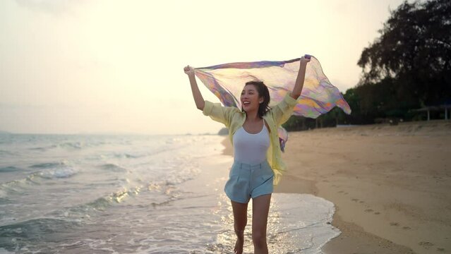 Happy Asian woman travel nature ocean on summer holiday vacation. Beautiful girl in casual clothing relax and enjoy outdoor lifestyle walking and relaxing on tropical island beach at summer sunset.