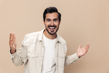 Portrait of a stylish man smile with teeth and surprise raised his hands up on a beige background in a white t-shirt, fashionable clothing style, copy space, space for text