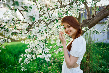 beautiful red-haired woman in a white dress smiling stands near a flowering tree