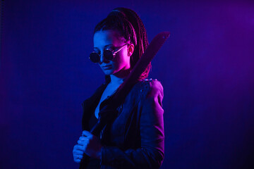 Young woman in a leather jacket in the dark with a machete knife in her hands. Neon light blue pink color. Rogue with melee weapons. - obrazy, fototapety, plakaty