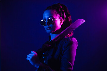 Young woman in a leather jacket in the dark with a machete knife in her hands. Neon light blue pink...