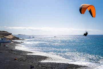 Unrecognizable paraglider lands on the Playa de la Enramada beach, a renowned paragliding spot in...