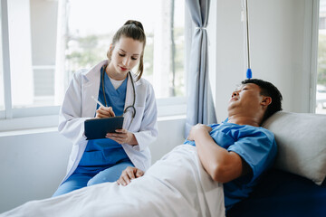  Doctor in white suit take notes while discussing and Asian elderly, man patient who lying on bed with receiving saline solution in hospital or clinic..