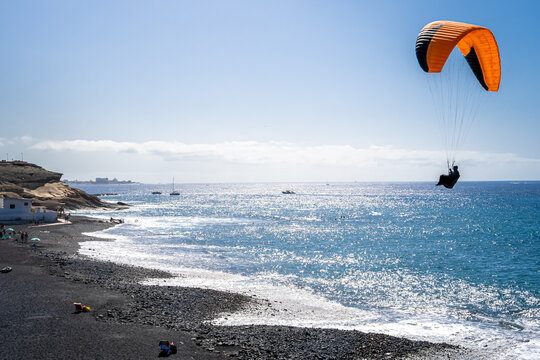 Unrecognizable paraglider lands on the Playa de la Enramada beach, a renowned paragliding spot in Tenerife, as the sparkling Atlantic Ocean serves as a picturesque backdrop, illuminated by sunlight.