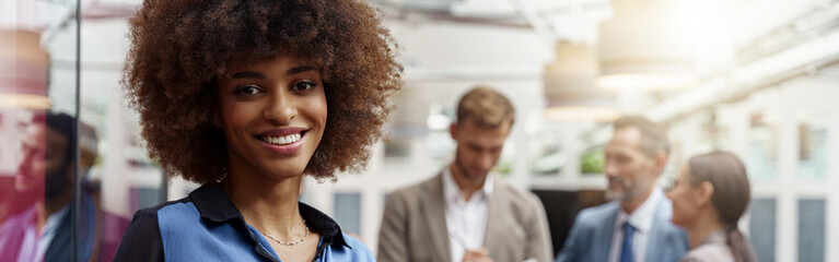 Smiling african businesswoman with laptop standing in modern office on colleagues background