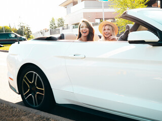 Portrait of two young beautiful and smiling hipster female in convertible car. Sexy carefree women...