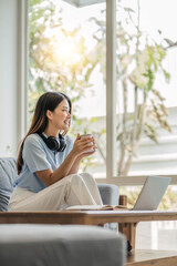 Fototapeta premium girl wearing headphones watching movies listening to music on laptop on the sofa at home on vacation with a cup of coffee