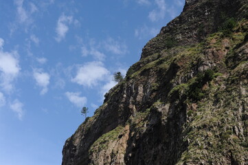 Steep mountain rock slope landscape with green trees an the top peak and blue sky and blue sky