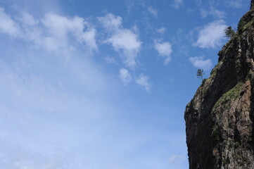 Steep mountain rock slope landscape with green trees an the top peak and blue sky and blue sky