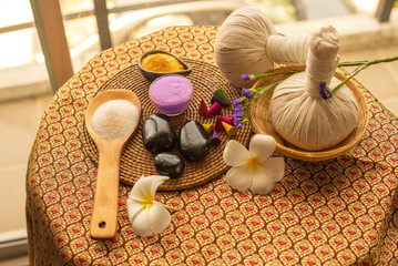 The spa composition of frangipani flower bowl with salt and herbal ball on the wooden table exudes a serene and calming ambiance.