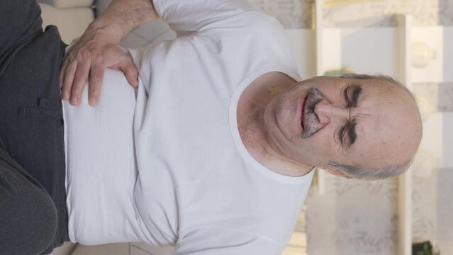 Vertical Video of Sick old man has stomach ache. Pancreatic Cancer.
The old man is sitting on the sofa at home and has stomach ache. Pancreas, stomach poisoning, chills.

