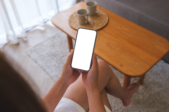Top view mockup image of woman holding mobile phone with blank desktop white screen at home