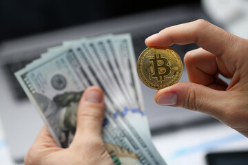Man hand holds one hundred dollar bills and golden bitcoin coin. Cryptocurrency income and financial investments