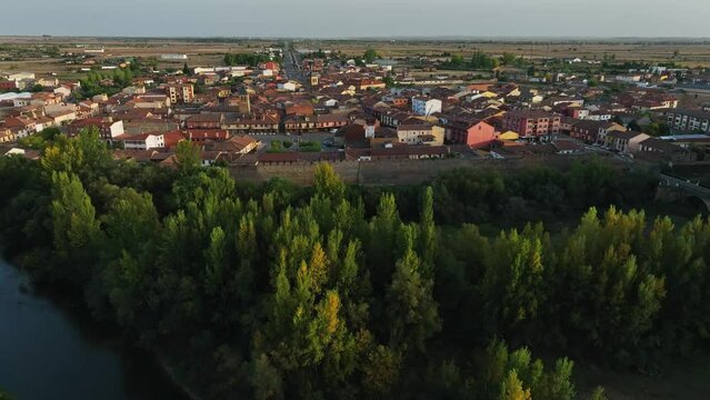 Drone flying backwards over river along banks of medieval Spanish town of Mansilla de las Mulas.