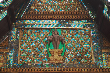 The stucco gable depicts Indra riding an Erawan elephant and vine patterns above the door edge of Wat Pa Ruak, an abandoned temple.