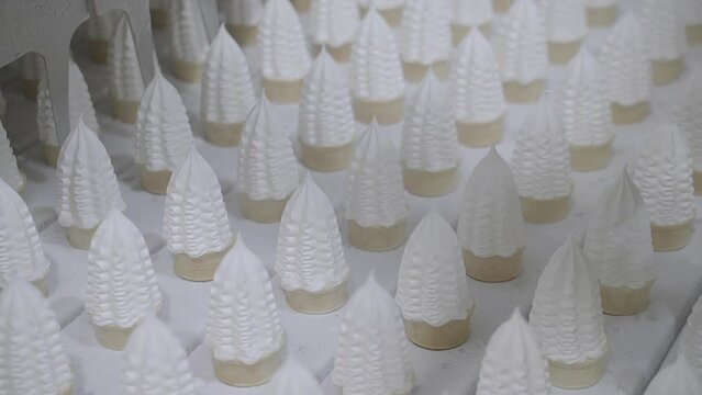 Close up clip of vanilla icecream cones being made on an industrial production line conveyor belt