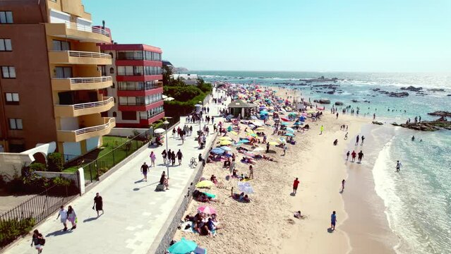 Drone fly over Pejerrey beach with people enjoying the last days of summer with buildings for tourism, Algarrobo, Chile.