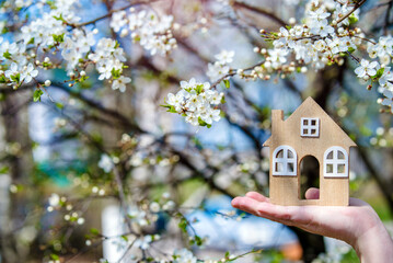 The girl holds the house symbol against the background of blossoming cherry
