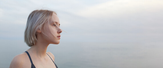 Naklejka premium Portrait of blonde woman standing on the background of blue sea and cloudy sky