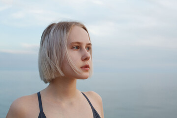 Naklejka premium Portrait of blonde pensive girl 17 years old on the background of blue sea and cloudy sky