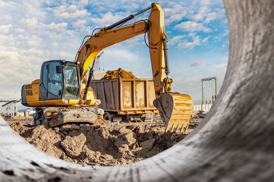 A wheeled excavator loads a dump truck with soil and sand. An excavator with a high-raised bucket against a cloudy sky View from the trench. Removal of soil from a construction site or quarry.