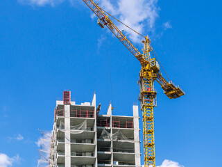 A tower construction crane on the background of a blue sky with clouds. The frame of a building under construction. Building construction. Load-bearing reinforced concrete walls of the house.