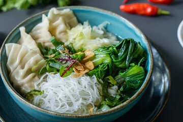A bowl of noodles with a bowl of green chilies and a plate of green chilies.