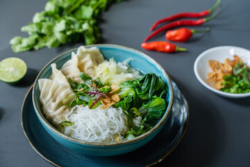 A bowl of noodles with a bowl of green chilies and a plate of green chilies.