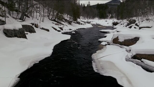 Aerial scenic drone forward reveal motion Canadian  wilderness mid winter near north Quebec Stoneham Ski Resort of frozen over Sautaurski River upstream