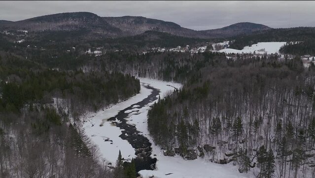 Aerial scenic drone pan up and forward Canadian  wilderness mid winter near north Quebec Stoneham Ski Resort of frozen over Sautaurski River with cozy cabin and chalets