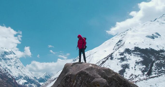 A mesmerizing orbit view of a man in a red jacket, shot by Drone, enjoying the stunning views of the huge Himalayan mountains and clouds during the Manaslu Circuit trek in Nepal.