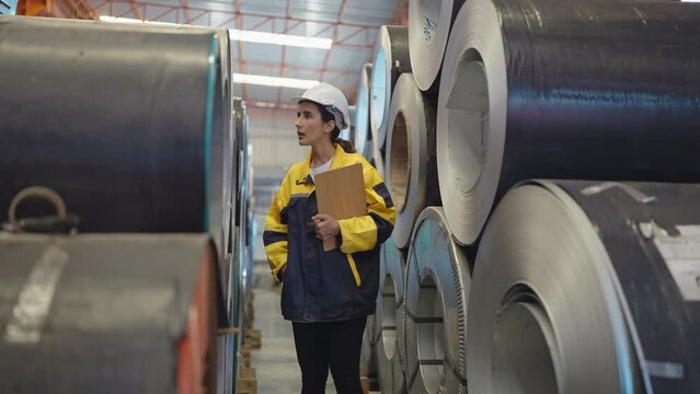 Hispanic Latino woman engineer wearing hard hat and uniform holding clipboard looking and checking aluminum rolls at the factory 