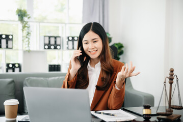 Asian female lawyer chatting online with client on laptop, smartphone  discussing details of lawsuit. in office.