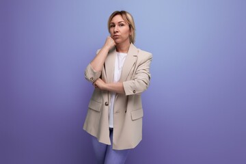 upset blond young business woman in jacket with arms crossed on studio background