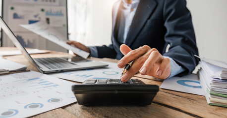 Close up Businessman using calculator and laptop for do math finance on wooden desk in office and business working background, tax, accounting, statistics and analytic research concept.