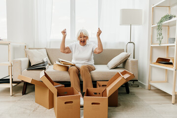 elderly woman sits on a sofa at home with boxes. collecting things with memories and moving and happiness smile.