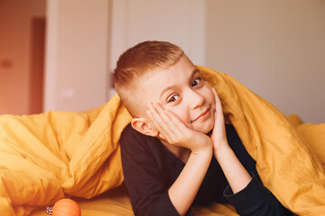 A joyful boy peers out from under the yellow blanket. The boy in his bad. Front view