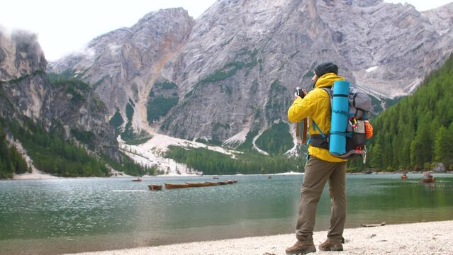 Young tourist hiker man taking pictures at beautiful alpine lake Lago Di Braies ,Pragser wildsee, in Trentino, Dolomites mountains, Italy.