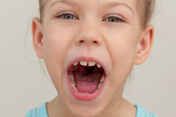 Child face with wide opened mouth cropped head caucasian little girl of 6 7 years on grey background