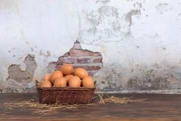Fresh eggs in basket laying on wooden floor, cement wall