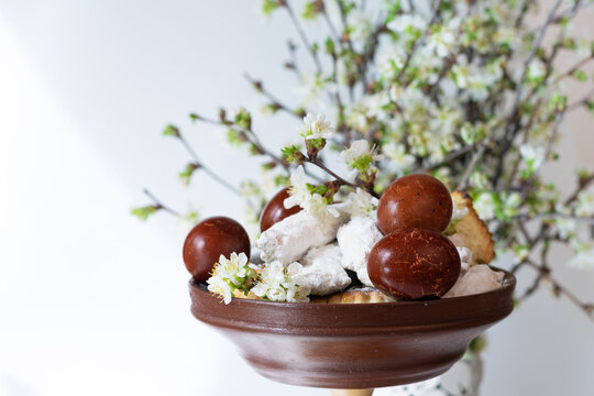 Easter decoration of wooden plate with baked goods and colorful eggs with background of blooming branches with white flowers, space for writing
