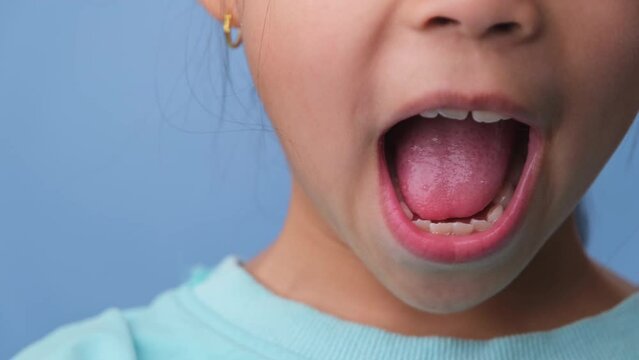 Close-up of smiling young girl revealing her beautiful white teeth on a blue background. Concept of good health in childhood.