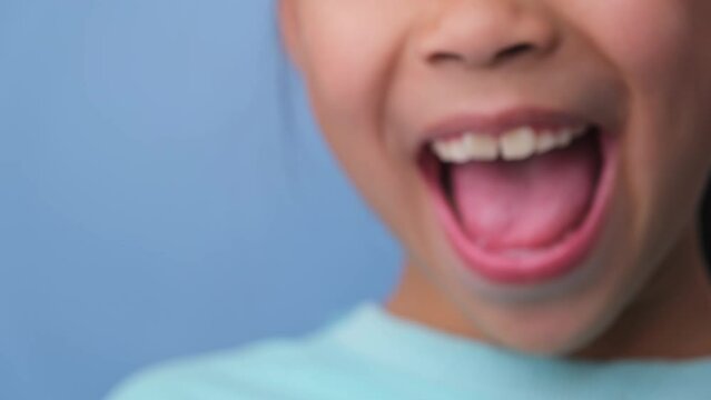 Close-up of smiling young girl revealing her beautiful white teeth on a blue background. Concept of good health in childhood.