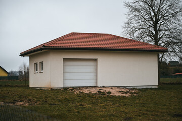 Obraz premium modern garage building with rolled white walls and a tiled red roof and a roller door. automobile hangar exterior with white gates.