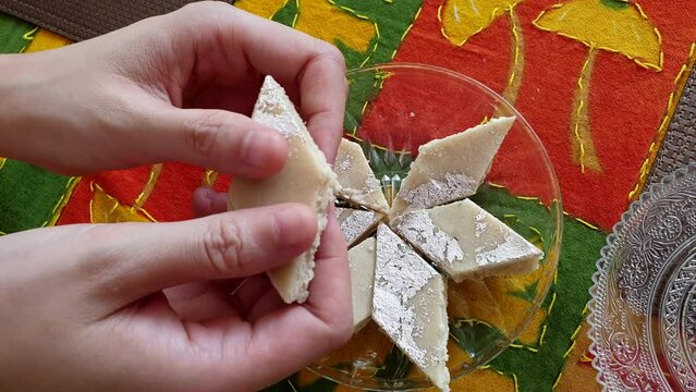 Hand picking breaking burfi barfi Indian sweet milk and cashew nut diamond cut bar with silver dairy milky India food