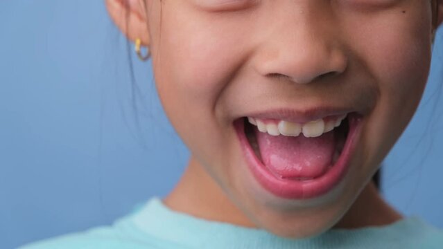 Close-up of smiling young girl revealing her beautiful white teeth on a blue background. Concept of good health in childhood.