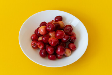 Fresh ripe cherries in a white plate on a yellow background. Close-up. Healthy food. Vegetarian breakfast.